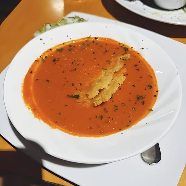A bowl of Matera Italian Restaurant's tomato soup, garnished with herbs and a cheese crisp.