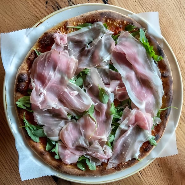 Matera Italian Restaurant & Bar's pizza topped with prosciutto and arugula on a wooden table.